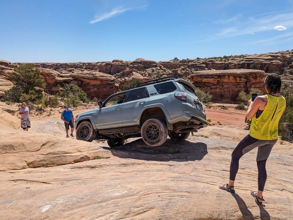several people surround a Toyota 4Runner with one rear wheel suspended high in the air as the SUV leans into a rocky descent