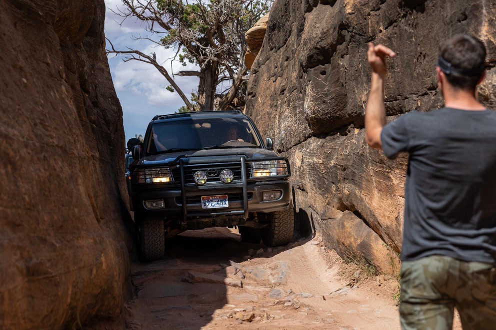 a spotter guides a Toyota Land Cruiser through an extremely narrow section between two sheer walls of sandstone