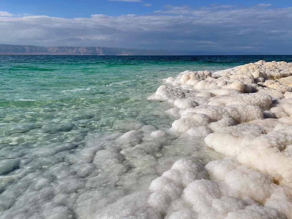 the turquoise waters of the Dead Sea lap over rocks completely encased by bright white salt
