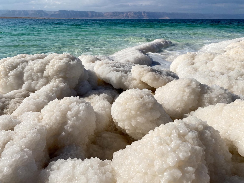 rocks covered in sharp white salt along the edge of the turquoise waters of the Dead Sea
