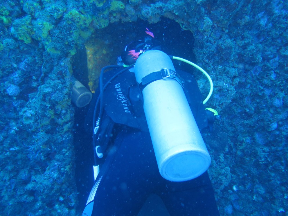 scuba divers swim through a coral-encrusted door opening into the USCG Duane