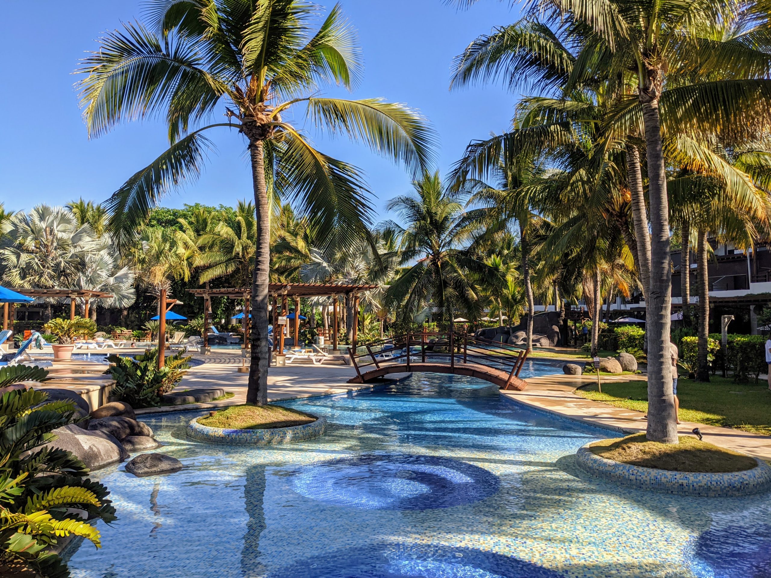 a beautiful tropical swimming pool complex stretches out in every direction with palm tress and bridges to help visitors move around