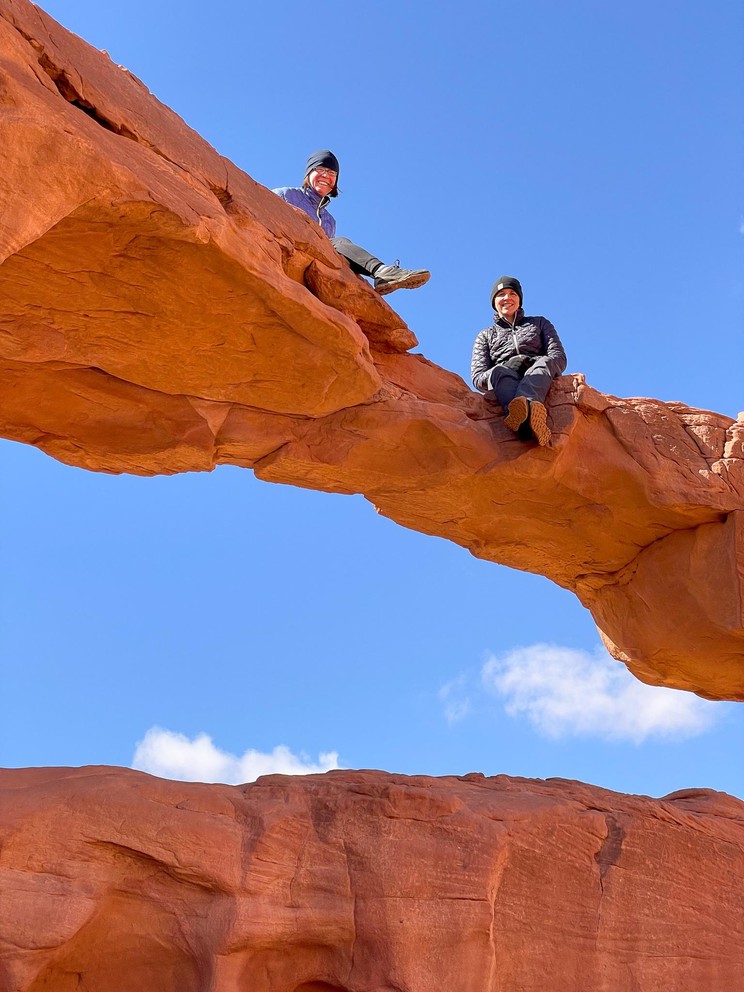 two women sit on top of a natural sandstone bridge