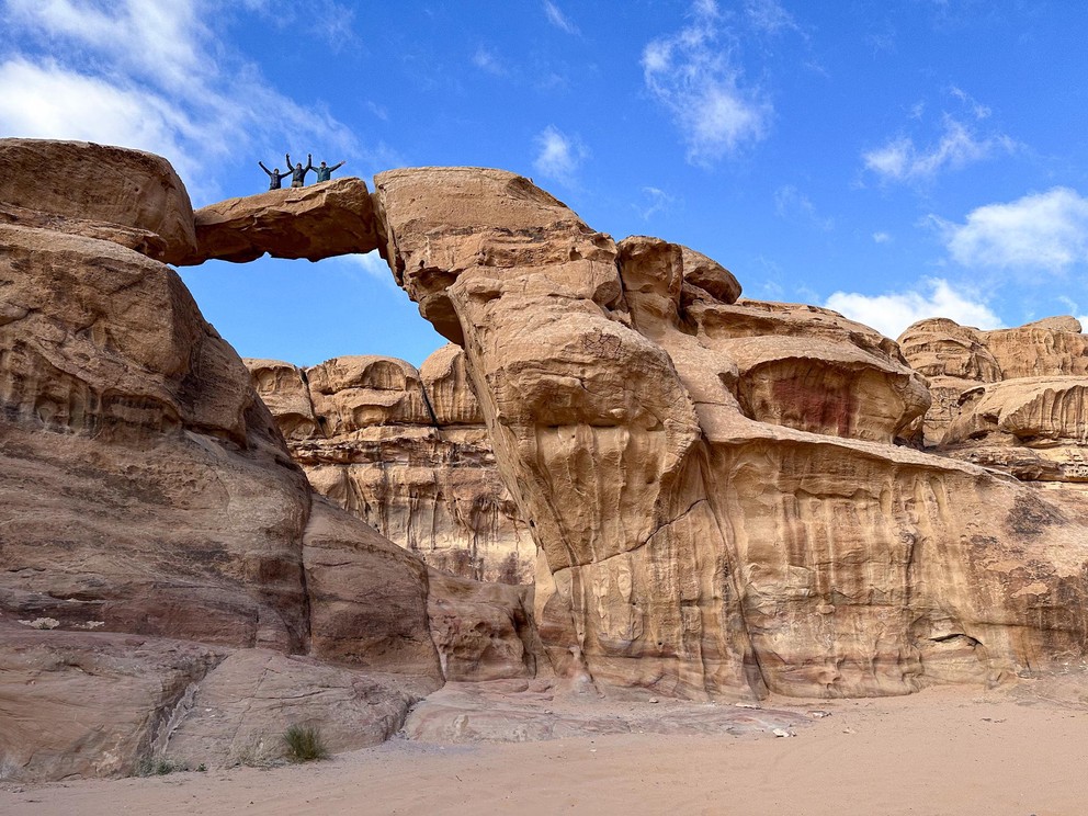 three people standing on top of a sandstone arch with their hands raised in celebration