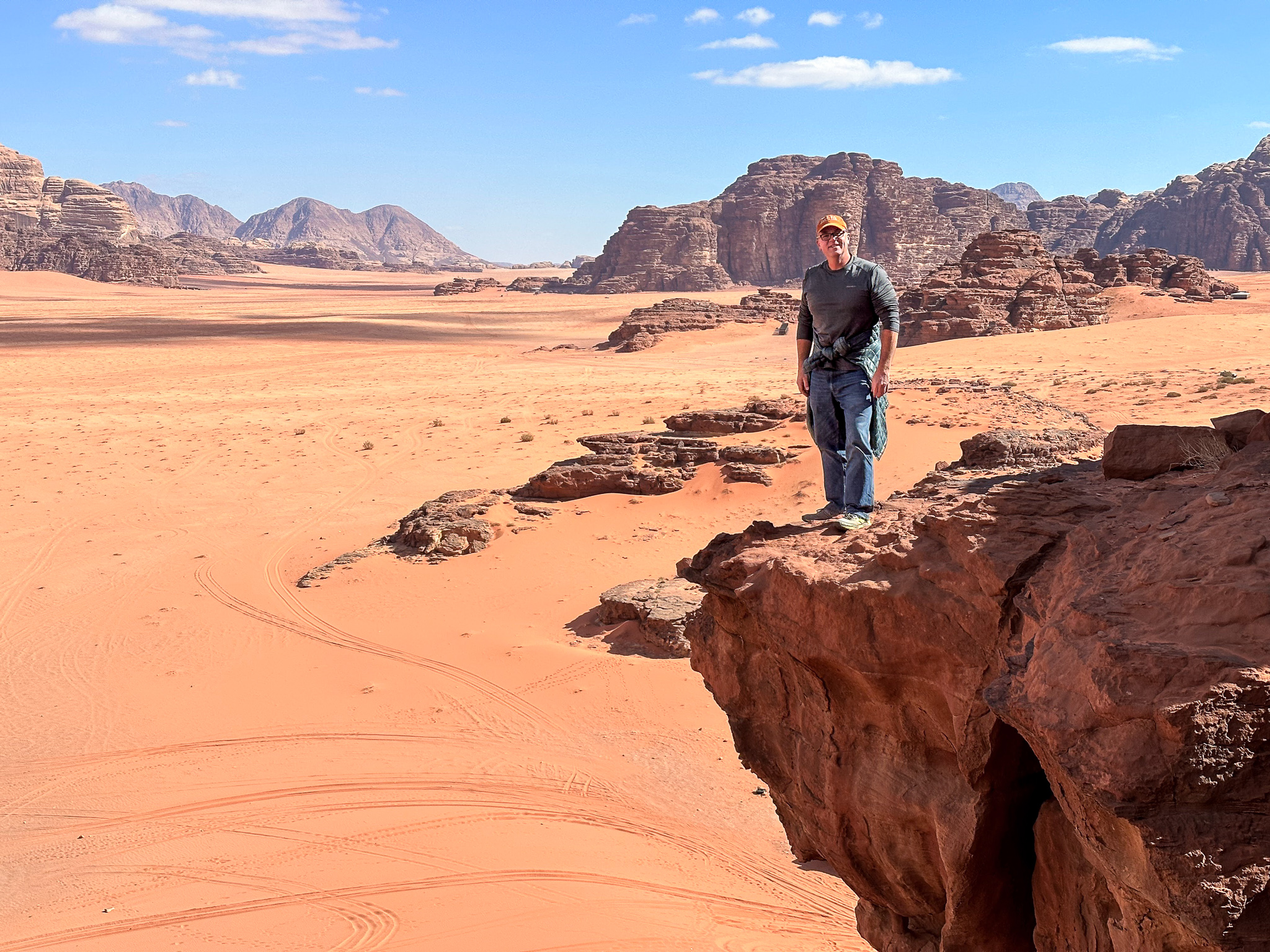 a man stands atop a rock overhanging the orange sands of Wadi Rum