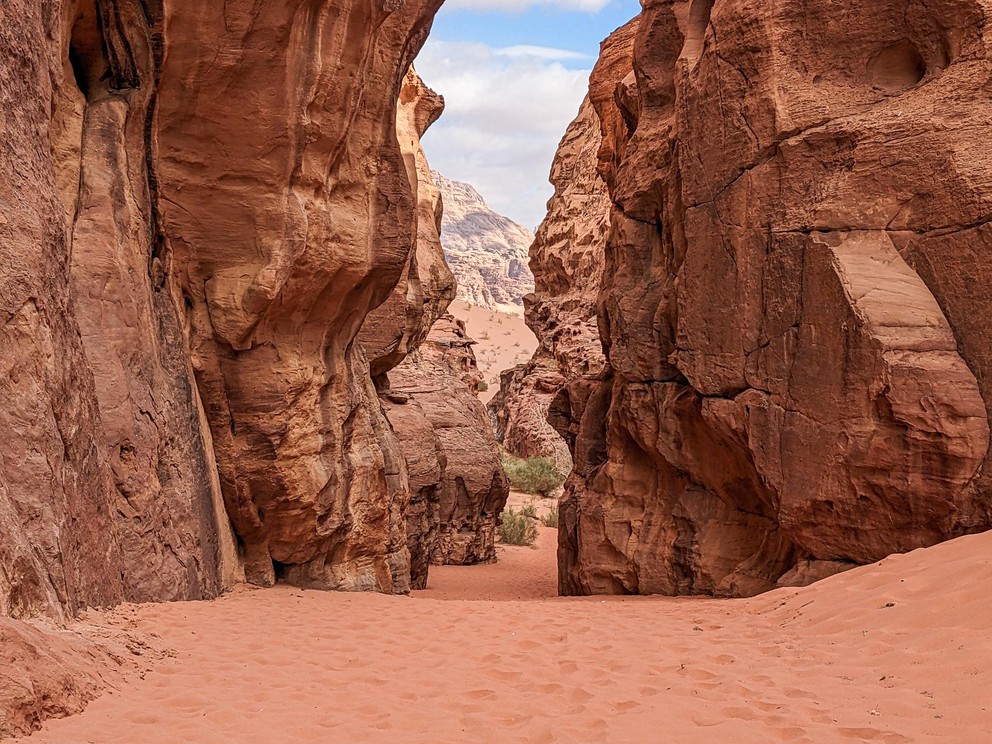 a sandstone canyon filled with red sand descends into a valley below