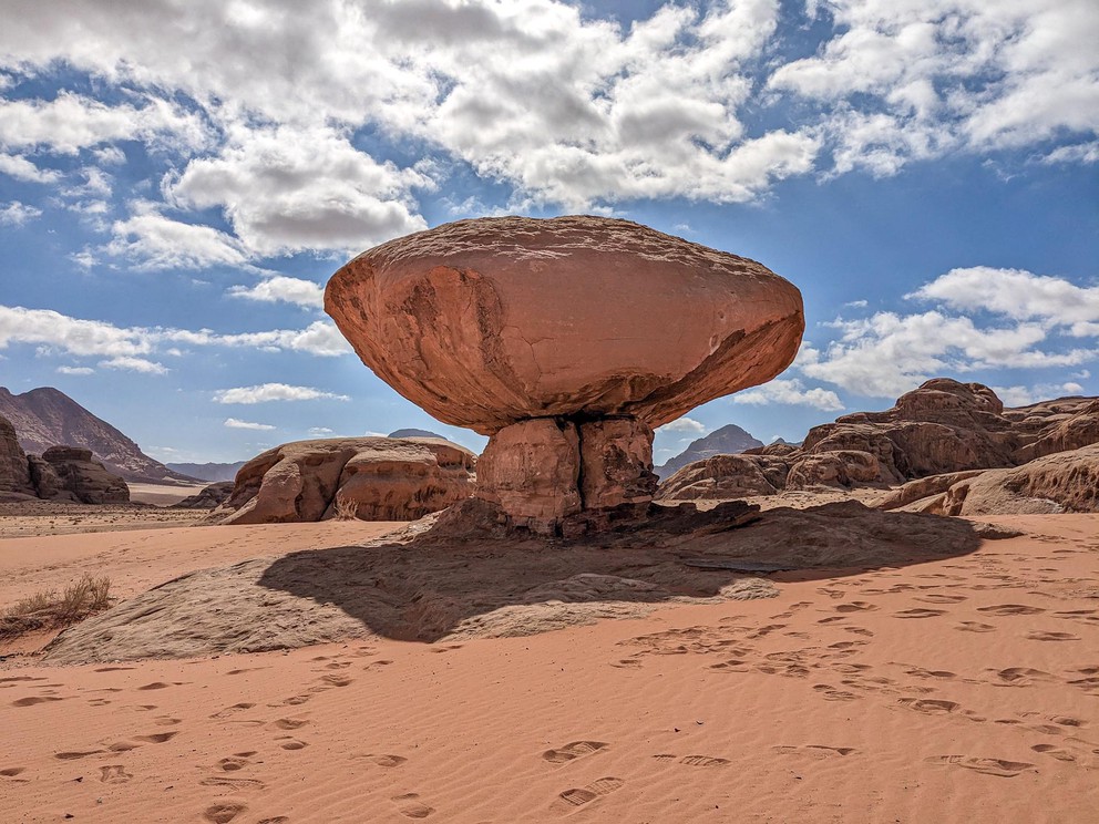 a sandstone rock shaped like a mushroom rises from the orange sand around it