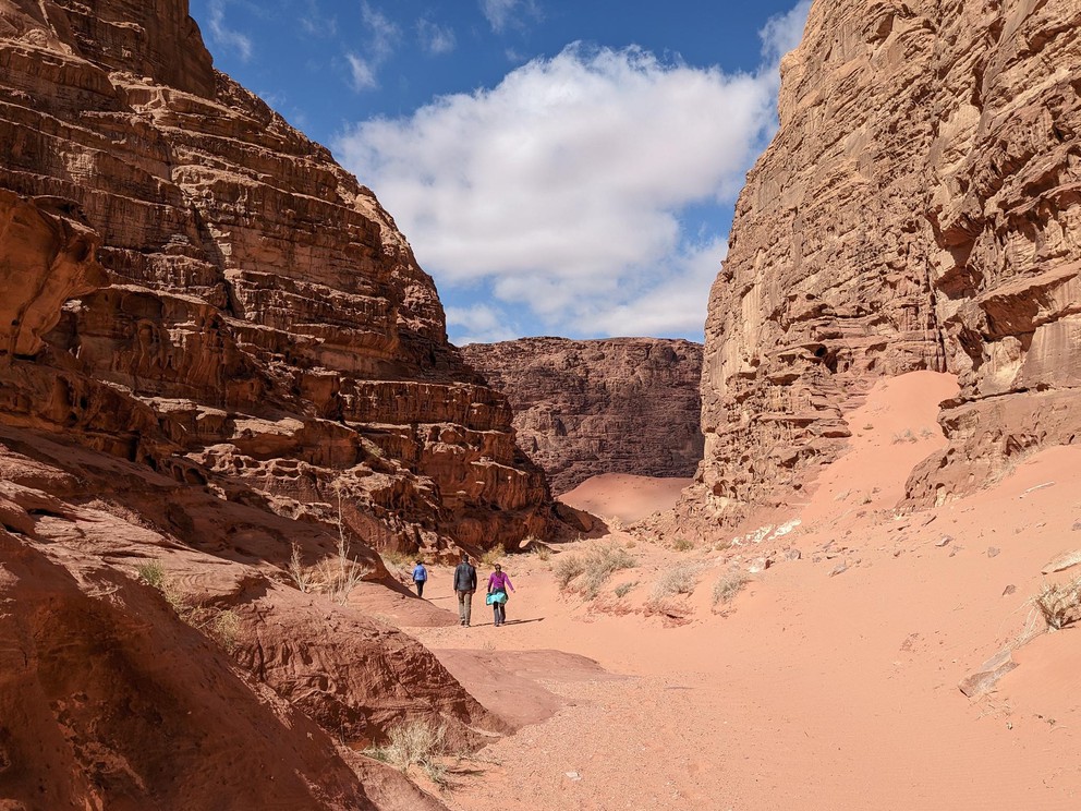hikers walk through a narrow sandstone canyon with sand drifts blown high against the canyon walls