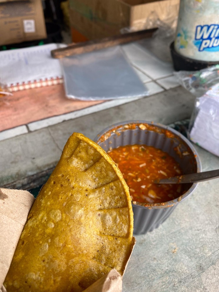one empanada held above a cup of red sauce