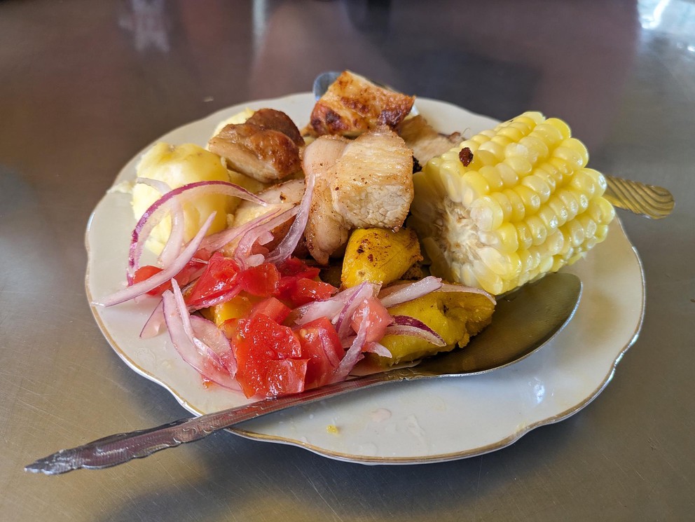 a small plate with chunks of pork, potato, corn, tomatoes, and onion
