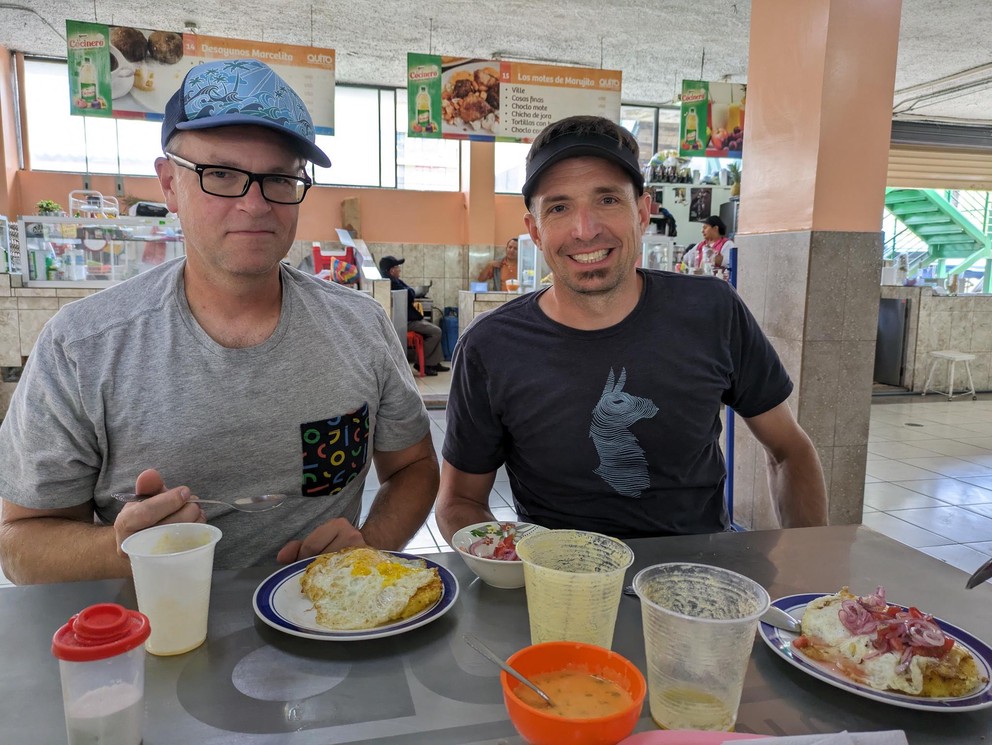 two men prepare to eat at a table inside a cafeteria
