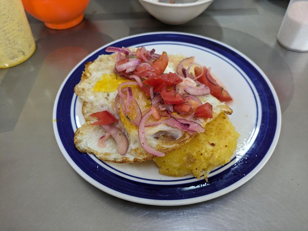 a plate with mashed yuca, fried eggs, and some diced tomato and onion