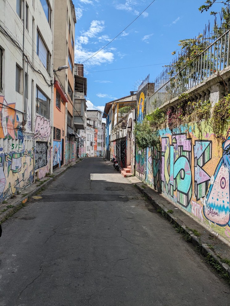 a narrow street with art painted on the walls as far as you can see