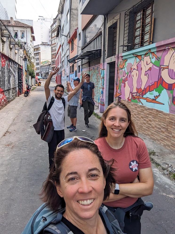 five people celebrate as they walk along art-filled streets in Quito