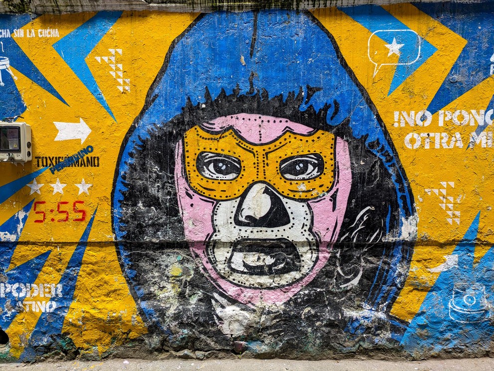 a mural of the face of a superhero wearing a luchador mask and hoodie