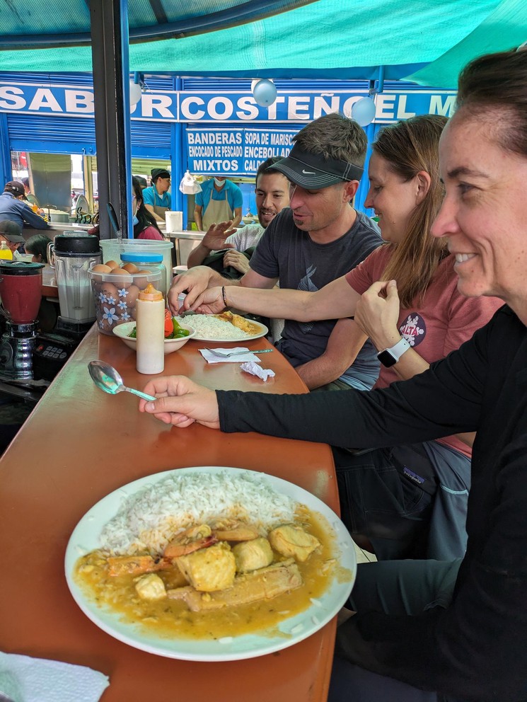 several tourists sit at a bar with plates of fish and rice before them