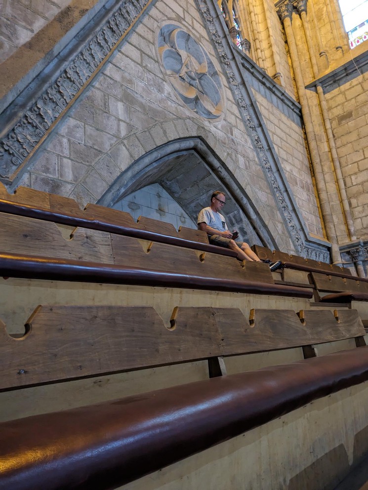 a man sits at the top of a row of pews and works on his phone