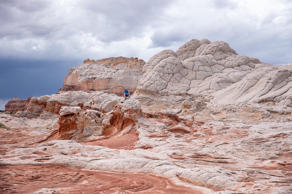 a woman sits atop white Navajo sandstone in what could be a sea of other sandstone formations