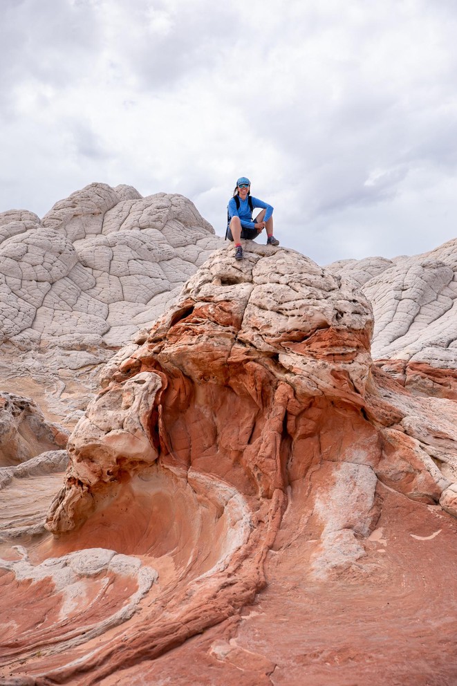 a woman smiles as she sits atop of a Navajo sandstone formation that looks like a boiling orange sea with white cauliflower rock all around