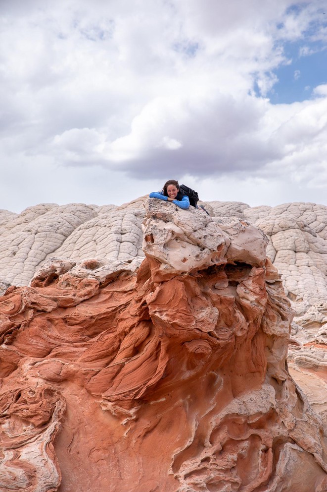 a woman rests on top of the a Navajo sandstone formation that appears to be a large stone bird with a red face and neck and a white crest on top