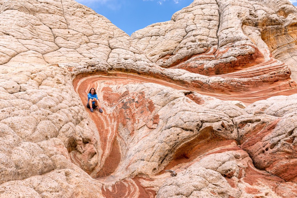 a woman sits on a narrow strip of red and white striped sandstone surrounded by white cauliflower rock - all Navajo sandstone formations